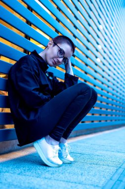 Bir duvara oturan kısa saçlı bir kadın