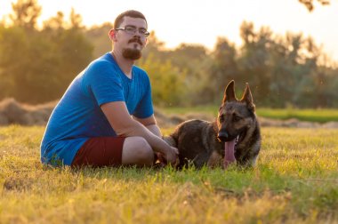 Yeşil gra üzerinde oturan bir adam ve bir Alman çoban köpeği görünümü