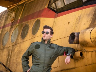 Eski bir uçağın yanında duran yakışıklı genç bir pilot.