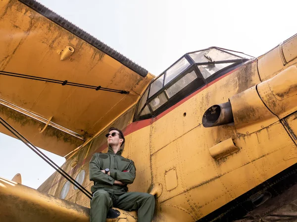 Un piloto joven y guapo sentado en el ala de un avión — Foto de Stock
