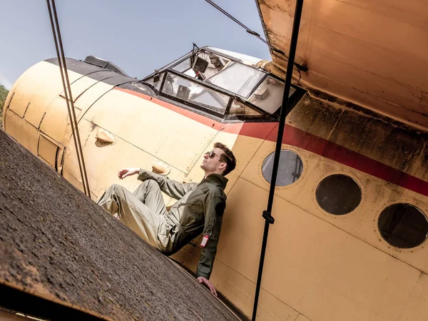 Un piloto joven y guapo sentado en el ala de un avión — Foto de Stock