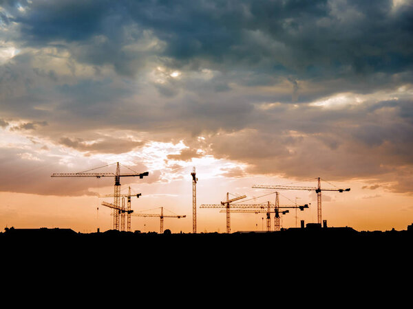 View on a consturction site with cranes during sunset with stormy clouds.