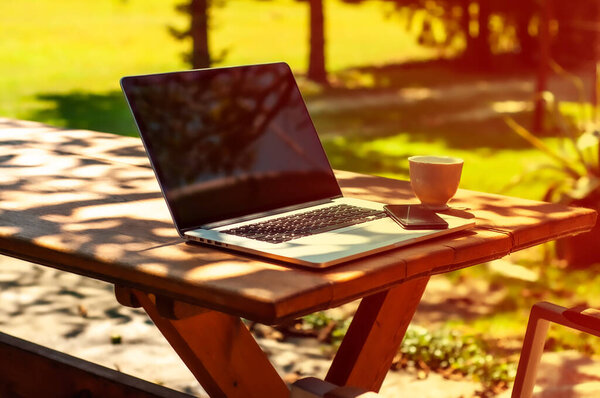View on a laptop pc and a smartphone and acoffee mug on a table in the garden in a home office or home school enviroment on a sunny day.