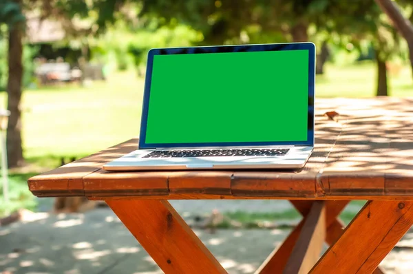 View on a laptop pc with a green screen on a table in the garden in a home office or home school enviroment on a sunny day.