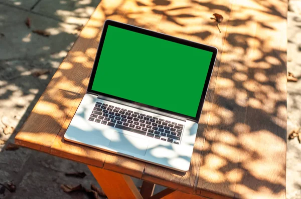 View on a laptop pc with a green screen on a table in the garden in a home office or home school enviroment on a sunny day.
