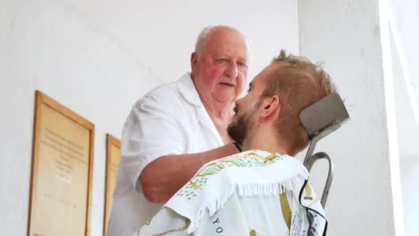 SZEKESFEHERVAR, HUNGRÍA - 22 DE JUNIO DE 2019: Un barbero tradicional afeitando a un joven con una navaja de afeitar en Szekesfehervar, Hungría durante el evento Festival de Hierro y Fuego. — Vídeos de Stock