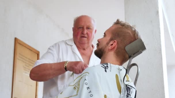 SZEKESFEHERVAR, HUNGRÍA - 22 DE JUNIO DE 2019: Un barbero tradicional afeitando a un joven con una navaja de afeitar en Szekesfehervar, Hungría durante el evento Festival de Hierro y Fuego. — Vídeos de Stock