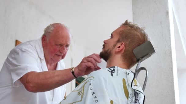 SZEKESFEHERVAR, HUNGRÍA - 22 DE JUNIO DE 2019: Un barbero tradicional afeitando a un joven con una navaja de afeitar en Szekesfehervar, Hungría durante el evento Festival de Hierro y Fuego. — Vídeos de Stock