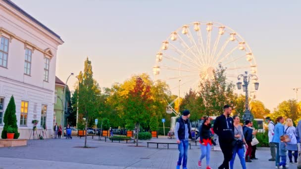 SEZKESFEHERVAR, HUNGARY - 10月26 、 2019:秋の日にハンガリーのSzekesfehervarの通りを歩く観覧車と人々を見る. — ストック動画