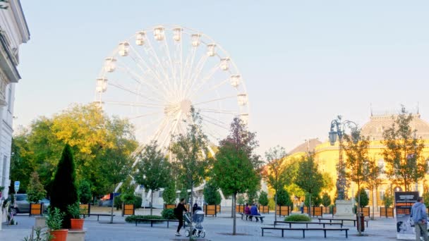 SEZKESFEHERVAR, HUNGARY - 10月26 、 2019:秋の日にハンガリーのSzekesfehervarの通りを歩く観覧車と人々を見る. — ストック動画