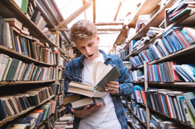 Duygusal öğrenci bir kütüphane atmosferik, eski anlamına gelir ve bir kitap okur. Genç bir adam şaşırmış gibi duygular ile parlak bir halk kütüphanesi bir kitap okur.