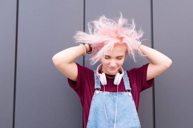 Mutlu sevimli kız komik pembe saç modeli ve gülümsüyor giderir. Pembe saçları, şık gençlik giyim ve karanlık bir duvar arka plan üzerinde kulaklık ile parlak, olumlu bir kız portresi.