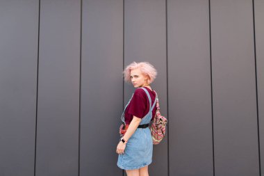 Genç parlak modeli arkasında bir sırt çantası ile karanlık bir duvar arka planı teşkil etmektedir ve kameraya benziyor. Şık bir kız gençlik giyim karanlık bir arka plan üzerinde duruyor