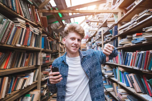 Handsome Young Man Stands Library Smearphone His Hand Shows His — Stock Photo, Image