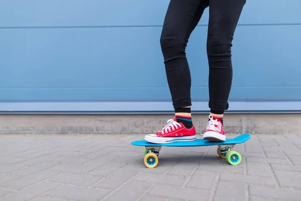 女孩与红色的家伙骑在蓝色的滑板的背景蓝色的墙壁 街道风格 特写腿 — 图库照片