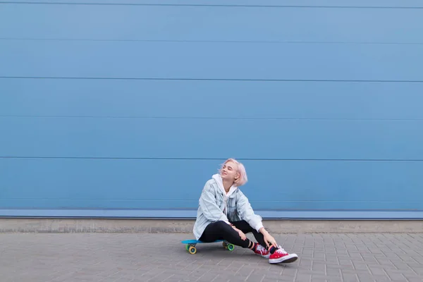 Menina Feliz Elegante Senta Skate Contra Uma Parede Azul Sorri — Fotografia de Stock