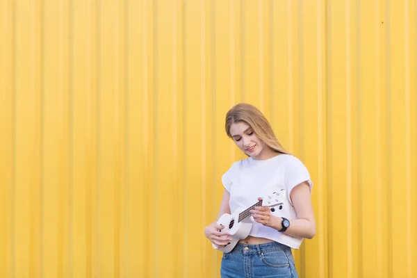 Menina Feliz Está Fundo Amarelo Joga Ukulele Sorri Conceito Musical — Fotografia de Stock