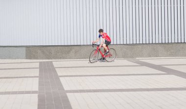 Bisiklete binme giysili genç adam bir minimalist modern ariculture arka plan üzerinde bir yol kırmızı bisiklet sürmek. Spor kavram. Bisiklet üzerinde yürümek.
