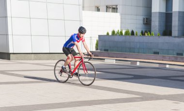 Delikanlı döngüsü giyim modern mimari bir arka plan üzerinde bir yol bisikleti sürmek. Spor kavram. Şehrin her yerinde bisikletçi döngüleri.