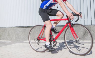 Kırmızı spor giyim gri duvar çerçevede bir kırmızı bisiklet sürmek bir bisikletçi yakın çekim portre. Bisiklet ve bacaklar yakın çekim. Spor kavramı.