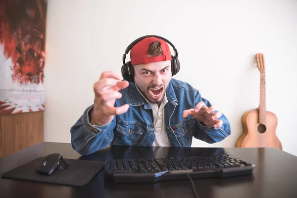 Portrait of an angry man playing computer games at home at the table. An emotional gamer plays games on a home computer and gets angry with defeat. Video Game Concept.