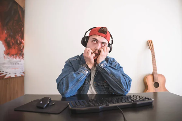 Αστείος Άνθρωπος Ένα Θλιμμένο Πρόσωπο Κάθεται Στον Υπολογιστή Στα Ακουστικά — Φωτογραφία Αρχείου