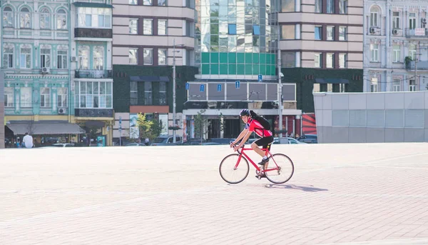 在城里骑一辆红色自行车的男子骑自行车的画像 一个骑自行车的红色运动衫和头盔骑在建筑背景的城市自行车 — 图库照片
