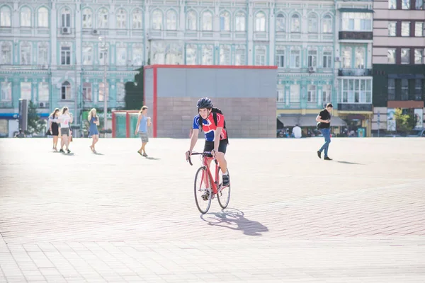 运动中的男子穿着一辆红色的自行车在城市与人和建筑学的背景 骑自行车的运动员骑车骑在城市广场上 — 图库照片