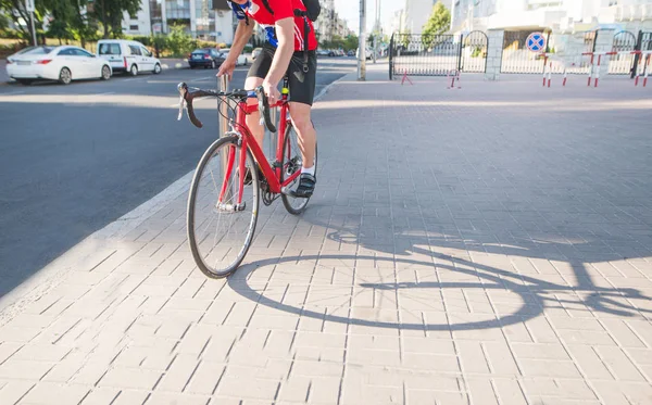 Professional cyclist in red sportswear is standing on a red bicycle on the sidewalk. Portrait racing driver of a cyclist. Sports concept.