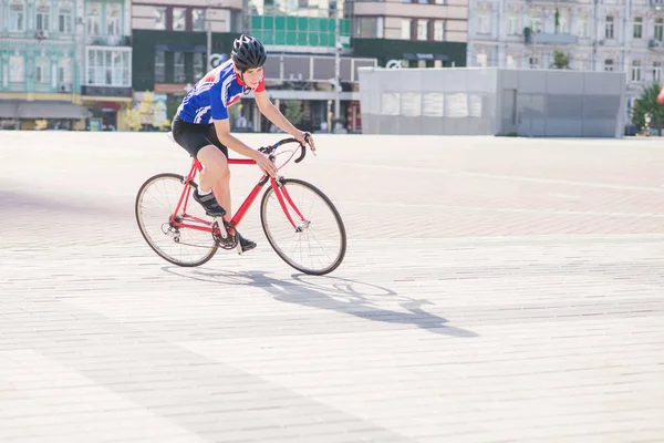 在建筑背景下 骑自行车的骑车人骑着一辆红色的公路车环游城市 一个穿着运动服和头盔的男人在城市广场骑自行车 — 图库照片