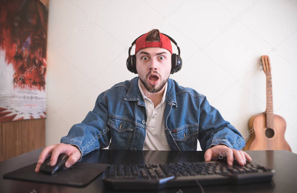 Amazed gamer with beard plays video games at home on a computer. Man with a surprised face sits at the table and plays video games. Portrait of a Surprised Gamer. Video Game Concept.