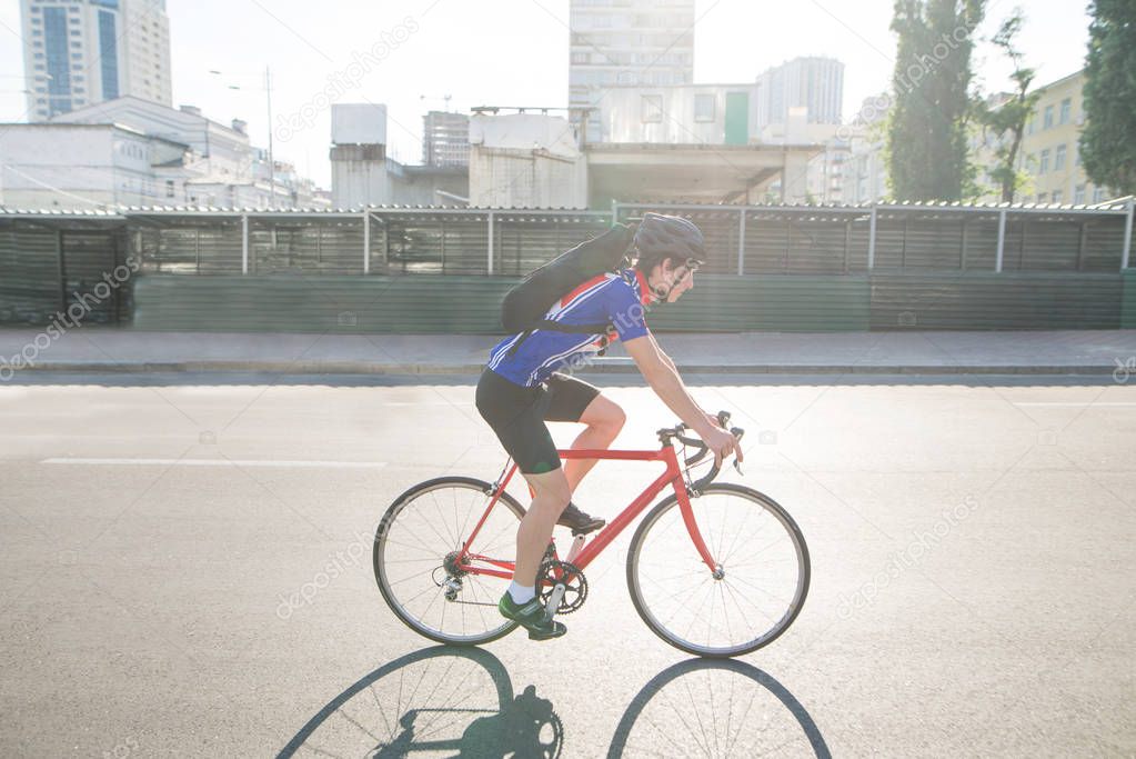 Portrait of an athlete cyclist who rides on the road in the city. Sports concept. A cyclist in sportswear and a helmet rides on a red bicycle road.