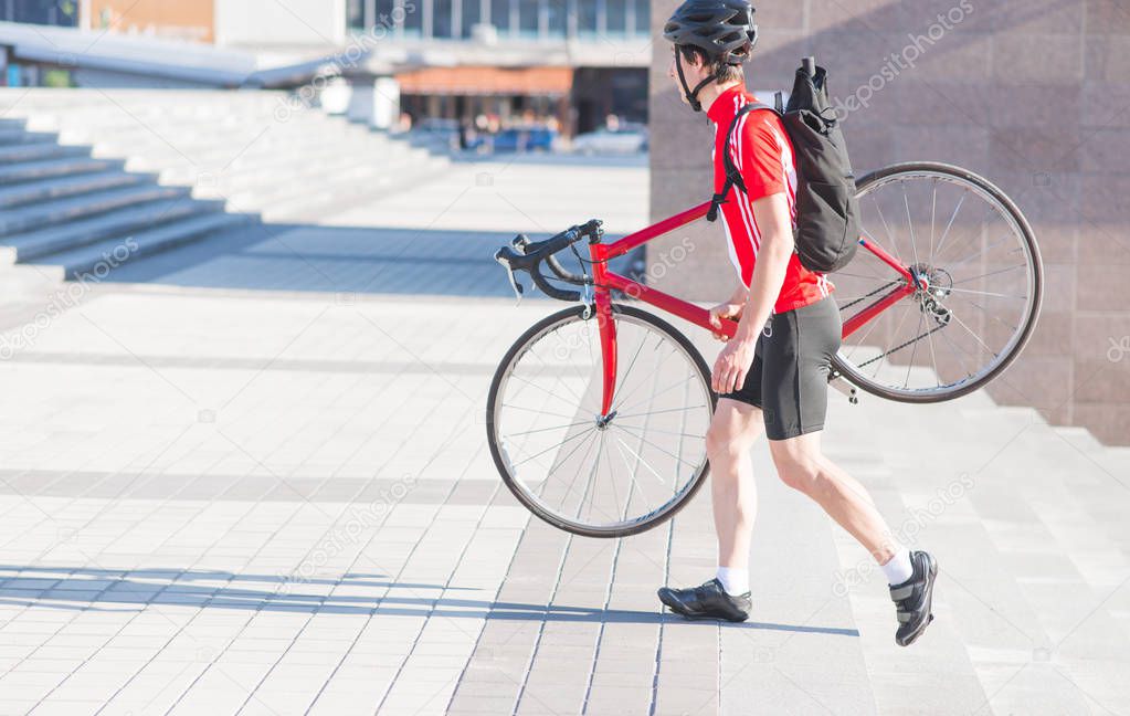 Man is a cyclist in sportswear, a helmet and a backpack on his back with a red bike in his hands down the stairs. Riding a city on a bike. Sports concept.