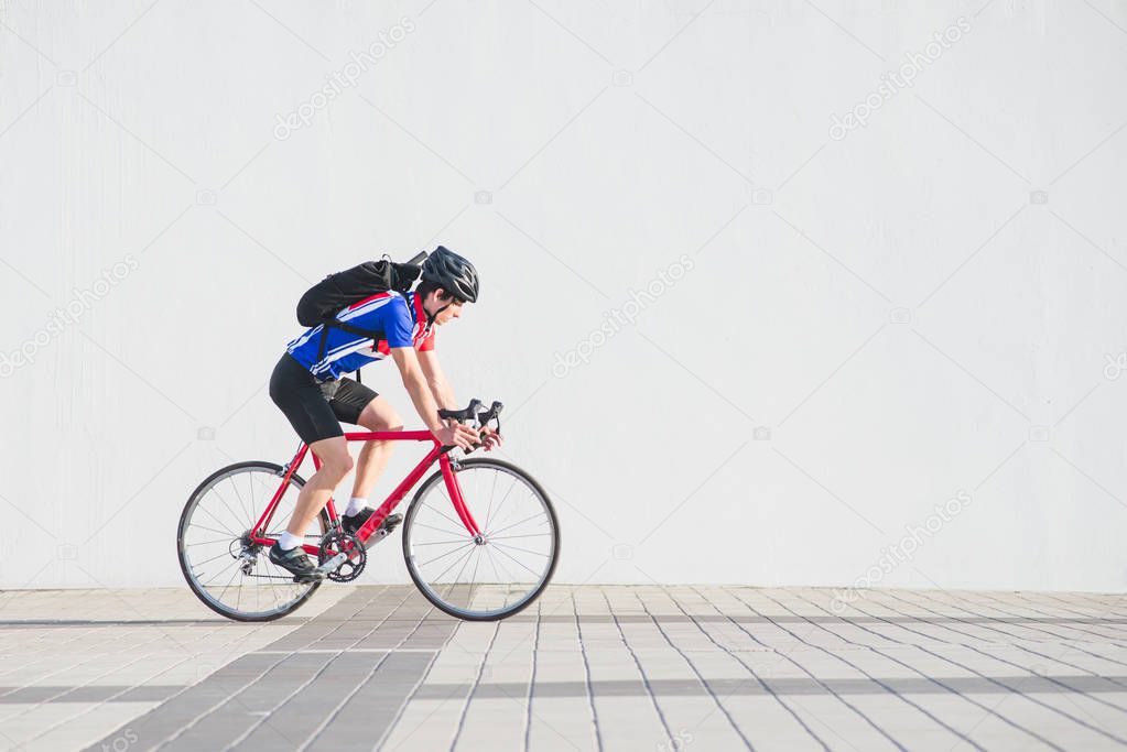 Cyclist in a helmet, athletic wear and a backpack on the back runs on the background of a white wall. Athlete bicyclist side view on the background of a light wall. Sports concept.