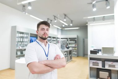 Parlak modern elektronik danışman portresi saklayın. Hansome Yardımcısı adam bir teknoloji Mağazası arka planda durur ve kameraya benziyor.
