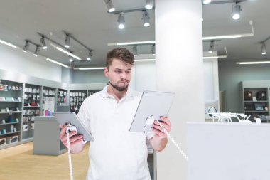 Yakışıklı adam elektronik mağazasında ile iki tablet elinde duruyor ve seçer. Seçin ve aygıtları elektronik mağazasında satın.