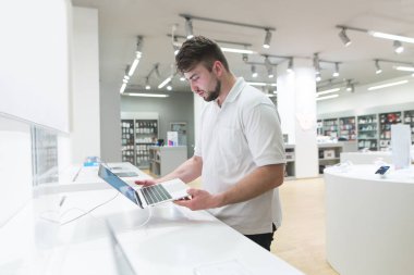 Bir dizüstü bilgisayar teknik mağaza arka planı onun elinde olan bir adam portresi. Alıcı bir dizüstü bilgisayar elektronik mağazasında seçer..