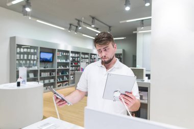 Handsome man chooses between two tablets in a modern technology store. The buyer is in the store and chooses which gadget to buy. clipart