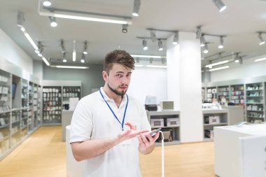 Teknoloji Mağazası Danışmanı ile bir akıllı telefon elinde duruyor ve kameraya benziyor. Işık elektronik elinde bir telefon Danışmanı portresi depolamak