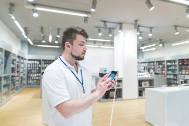 Bir smartphone gösterilen Teknoloji Mağazası Danışmanı portresi. Danışman ile modern, hafif elektronik arka planı elinde bir vaaz depolamak.
