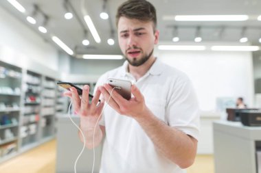 adam modern bir mağazada iki akıllı telefonlar arasında seçer. Alıcı bir akıllı telefon elektronik mağazasında seçer. Gadget'ları satın alma.