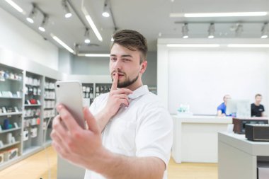 Yakışıklı adam akıllı bir teknoloji Mağazası bir sephi yapar. Alıcı bir smartphone cep telefonu ile ön kamera testleri. Elektronik mağazasından bir akıllı telefon satın almak.