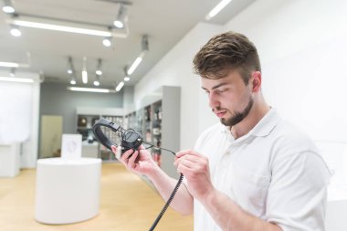Yakışıklı adam kulaklık modern elektronik mağazasında seçer. Alıcı arka plan ışık mağaza, kulaklık bakar. Satın alma kulaklıklar.