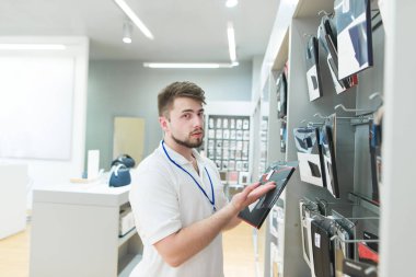 Teknik mağazanın becerikli alet aksesuarları bölümünde danışmandır. Modern Elektronik Mağazası beyaz T-shirt danışman tablet ve diğer araçlar için aksesuarlar sunuyor.