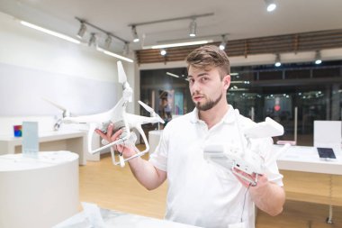 Bir quadcopter ve bir denetleyici bir ışık Teknoloji Mağazası olan bir adam portresi. Bir adam bir dron quadcopter deposunda seçer ve kameraya benziyor