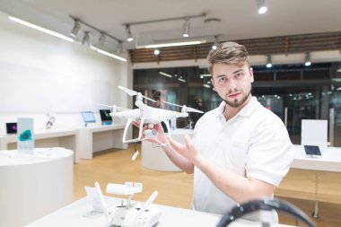 Yakışıklı bir quadcopter ile modern bir mağazada onun elinde duruyor ve kameraya benziyor. Quadcopter robotları mağazasından satın