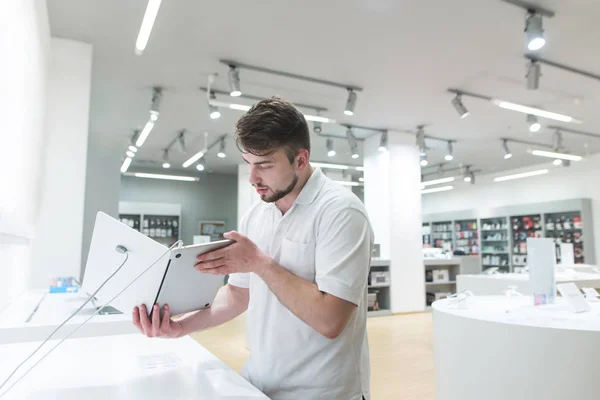 Handsome man looks at a notebook in a light tech store. A buyer chooses a notebook in a modern electronics store. Purchase a gadget.