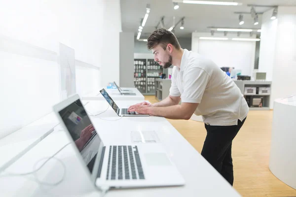 Man uses a laptop in the computer department of the technology store. Showcase with laptops. The buyer selects a gadget in the notebook department.