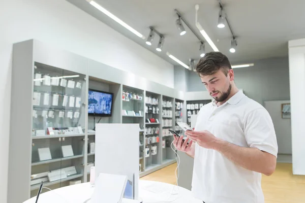 Handsome bearded man is in the electronics store in the phone department and chooses a smartphone. Buyer buys a smartphone in a technology store. Purchase of a smartphone in a technology store.