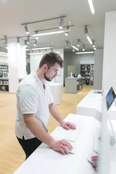 Man uses a computer in a modern electronics store. Buyer selects a monoblock in a light technology store. Buy a computer. Purchase monoblock. Choosing a computer in the store.